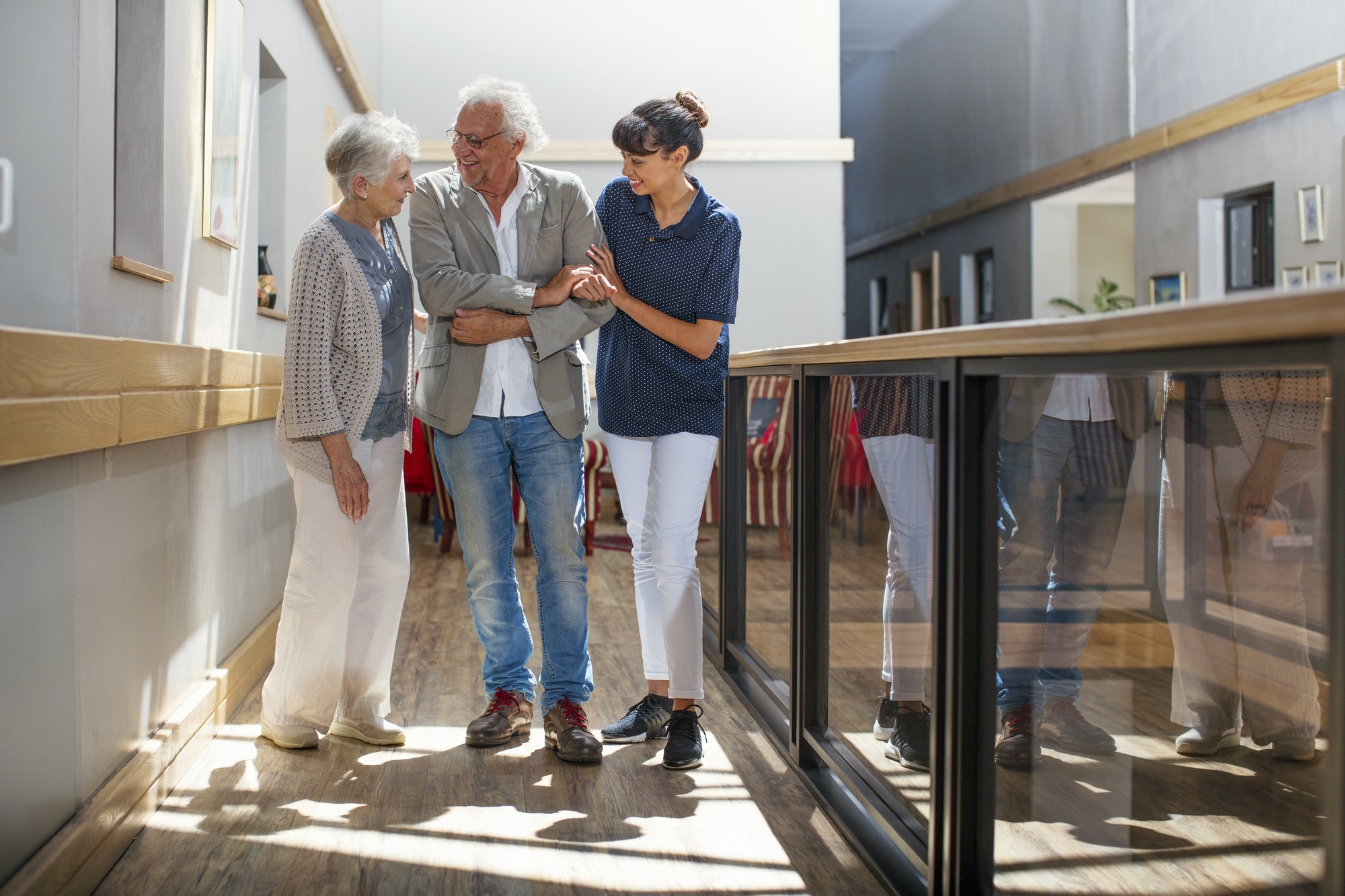 Gereatric nurse helping senior man and woman to walk down corridor